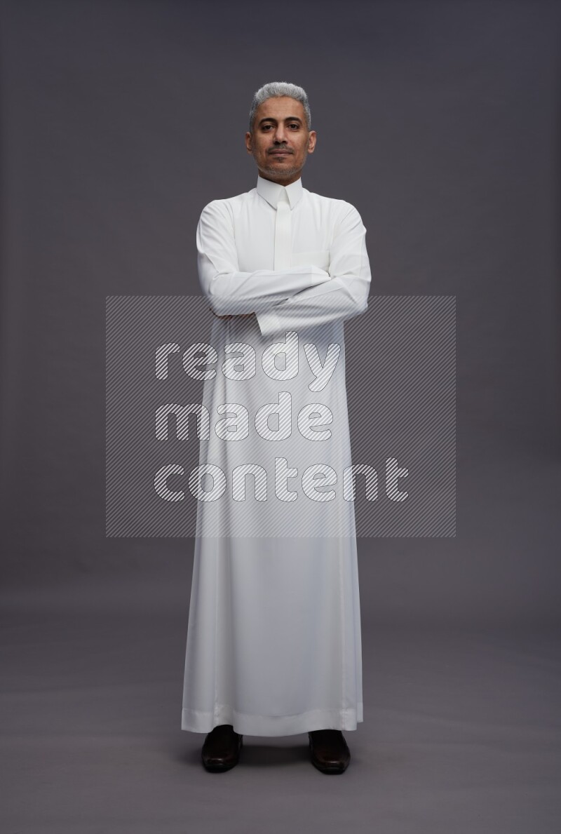 Saudi man wearing thob standing with crossed arms on gray background