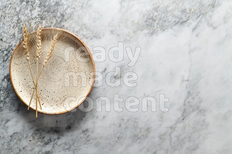 Wheat stalks on Multicolored Pottery Plate on grey marble flooring, Top view