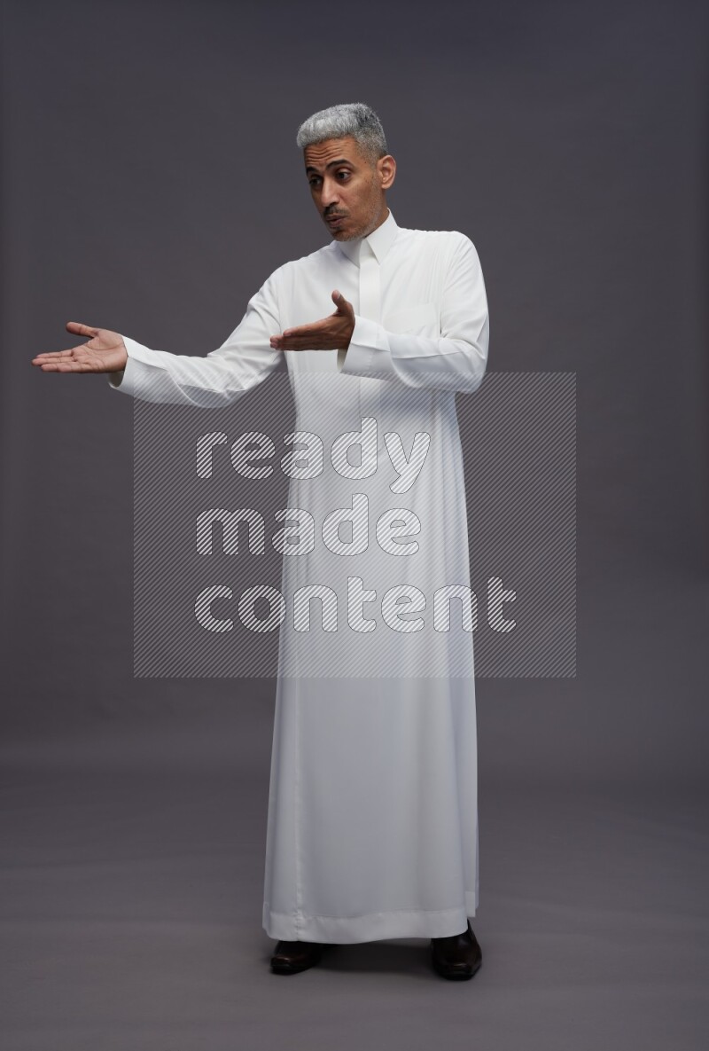 Saudi man wearing thob standing interacting with the camera on gray background