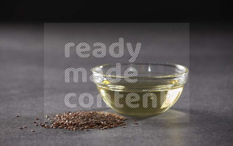 وعاء زجاجي ممتلئ بزيت بذر الكتان مع بعض حبوب بذر الكتان بجانبه علي خلفية سوداء