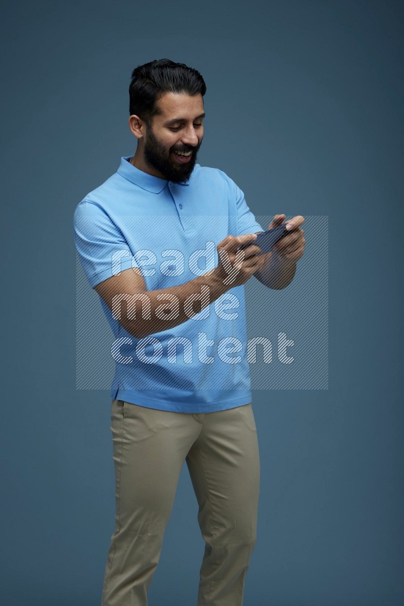 Man playing a game on his phone in a blue background wearing a Blue shirt