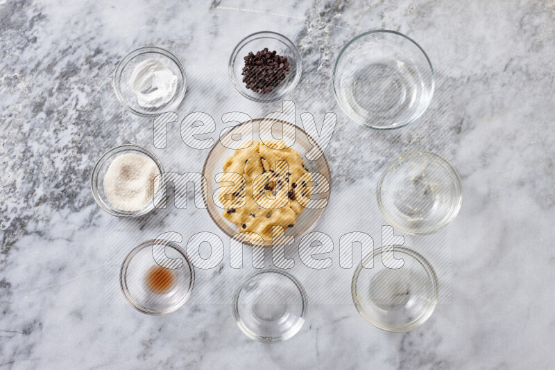 Cookies step by step with its ingredient, flour, butter, brown sugar, egg, vanilla extract, white sugar, chocolate chips and baking soda on grey marble background