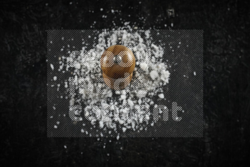A wooden grinder standing upright and surrounded by coarse white sea salt on black background