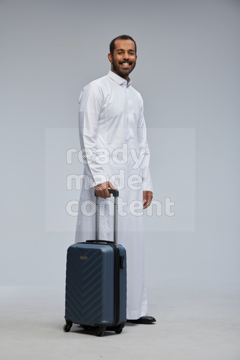 Saudi man wearing thob standing holding Travel bag on Gray background