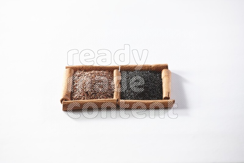 مربعان من أعواد القرفة ممتلئان ببذور الكتان وحبة البركة السوداء علي خلفية بيضاء