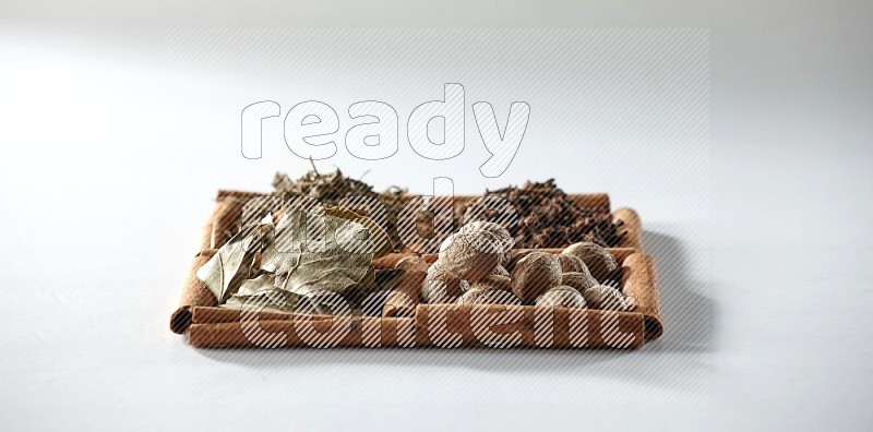 4 squares of cinnamon sticks full of bay laurel leaves, dried basil, cloves and nutmegs on white flooring