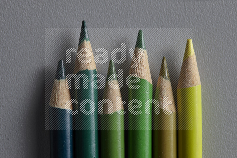A collection of colored pencils arranged showcasing a gradient of green hues on grey background