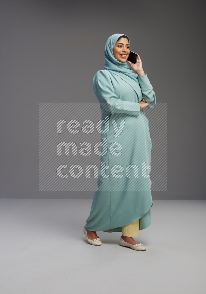 Saudi Woman wearing Abaya standing talking on phone on Gray background
