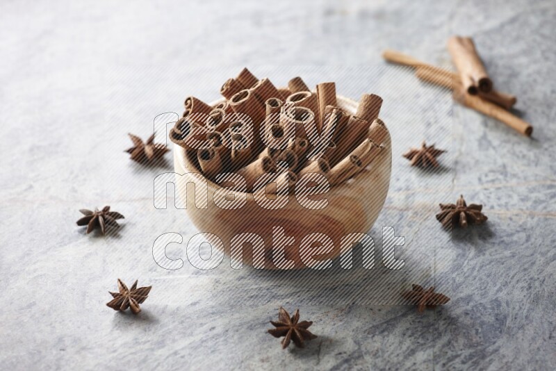 wooden bowl full of cinnamon sticks surrounded by star anis on marble background in different angles