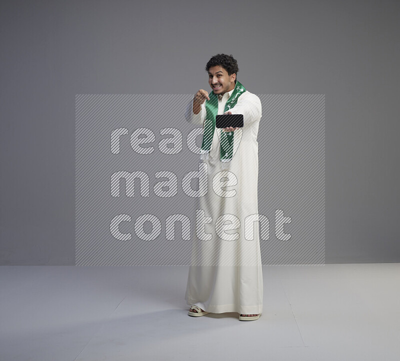 رجل سعودي يرتدي ثوب ابيض و شال يحمل جوال