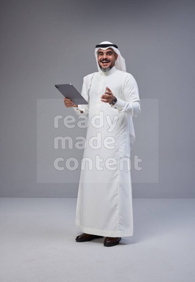 Saudi man Wearing Thob and white Shomag standing working on tablet on Gray background