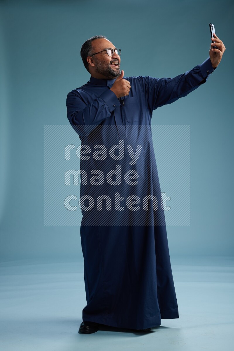Saudi Man without shimag Standing taking selfie on blue background