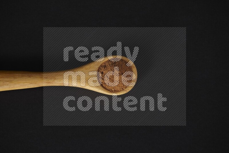 Cinnamon powder in a wooden spoon on a black background