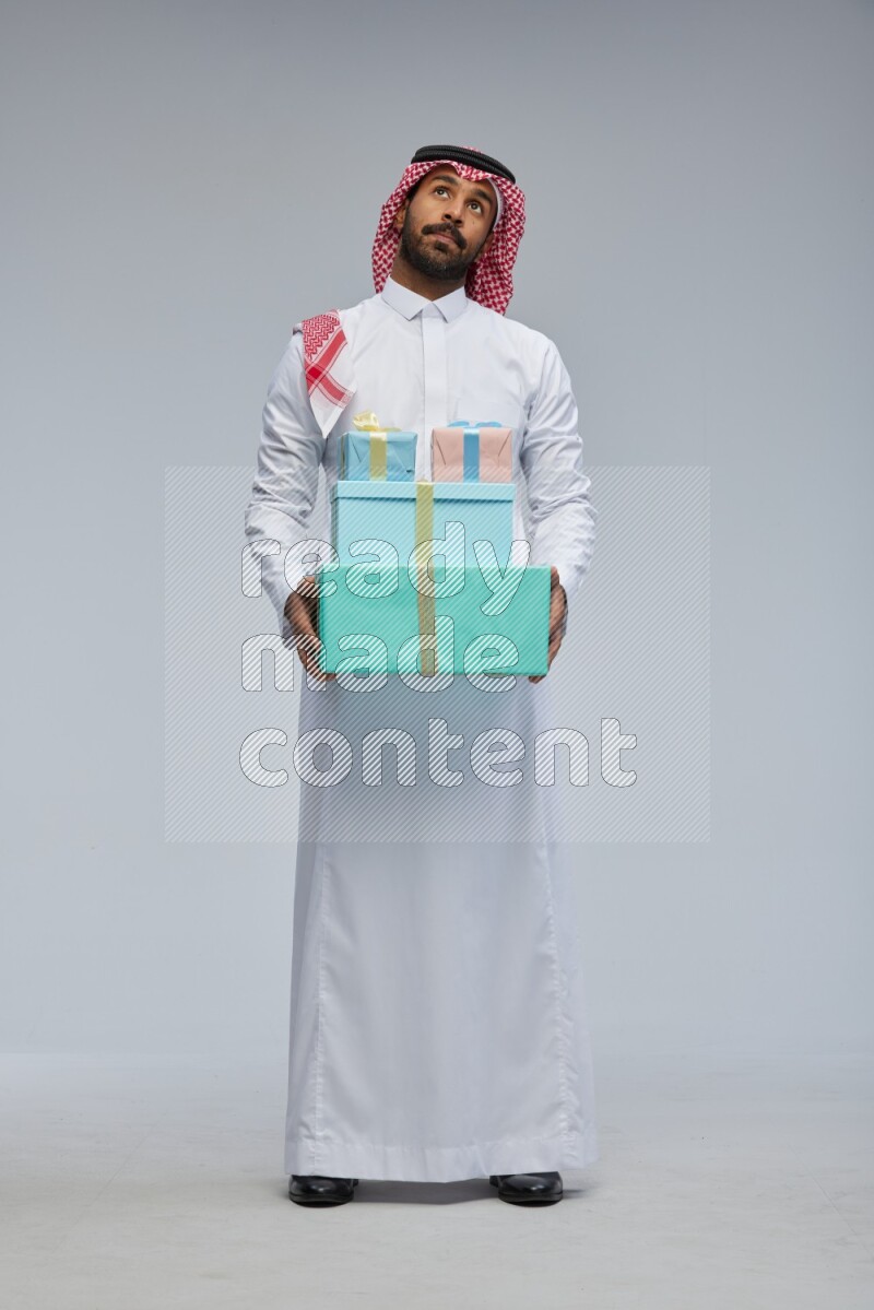 Saudi man Wearing Thob and shomag standing holding gift box on Gray background