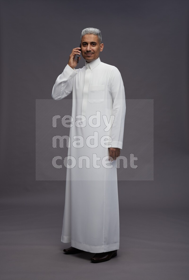 Saudi man wearing thob standing talking on phone on gray background