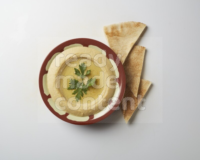 Hummus in a traditional plate garnished with parsley on a white background