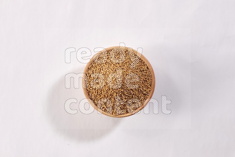 A wooden bowl full of mustard seeds on a white flooring