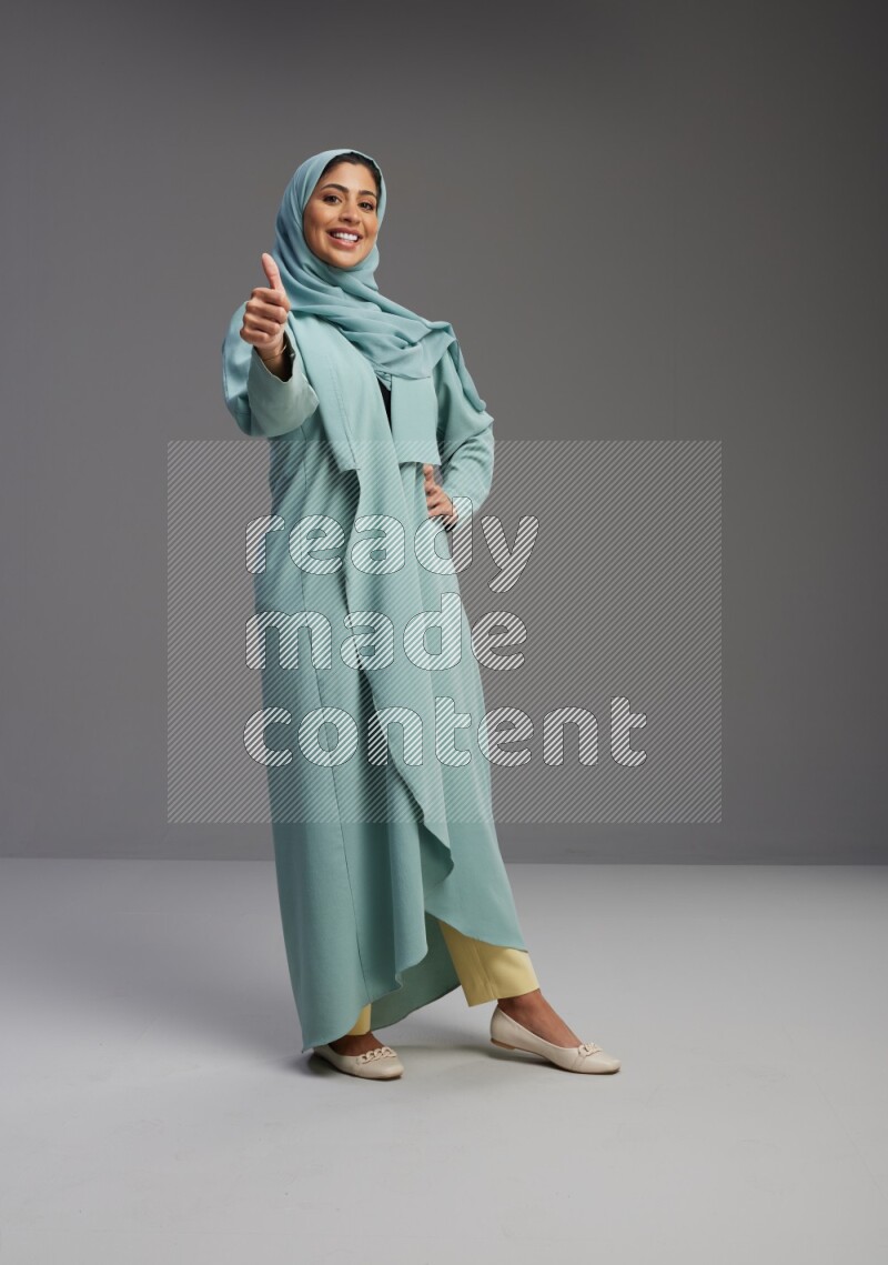 Saudi Woman wearing Abaya standing interacting with the camera on Gray background