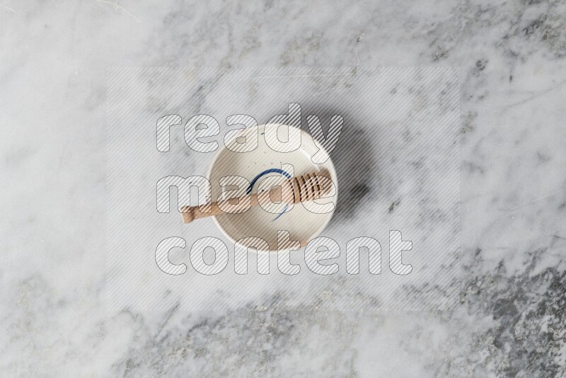 Multicolored pottery bowl with wooden honey dipper in it on grey marble background