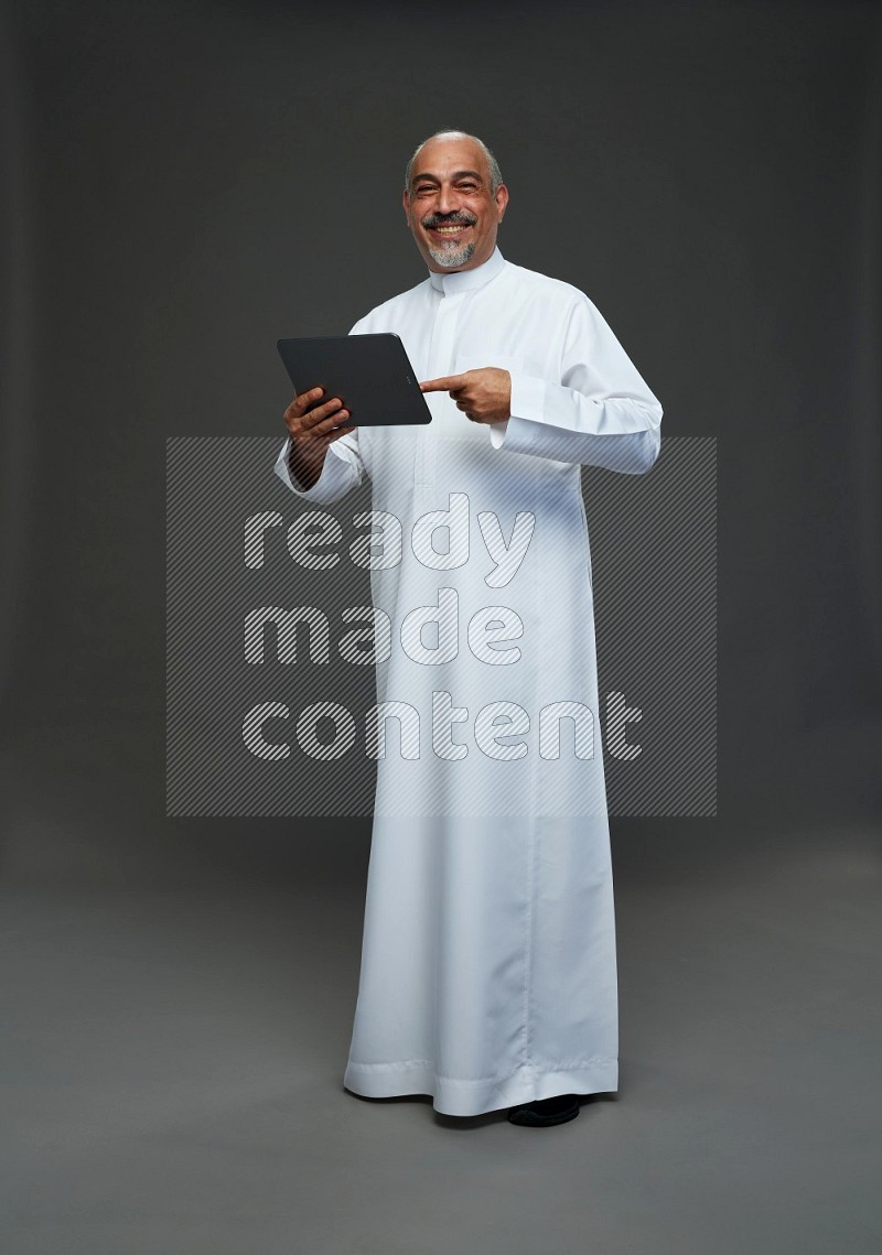 Saudi man without shomag Standing working on tablet on gray background