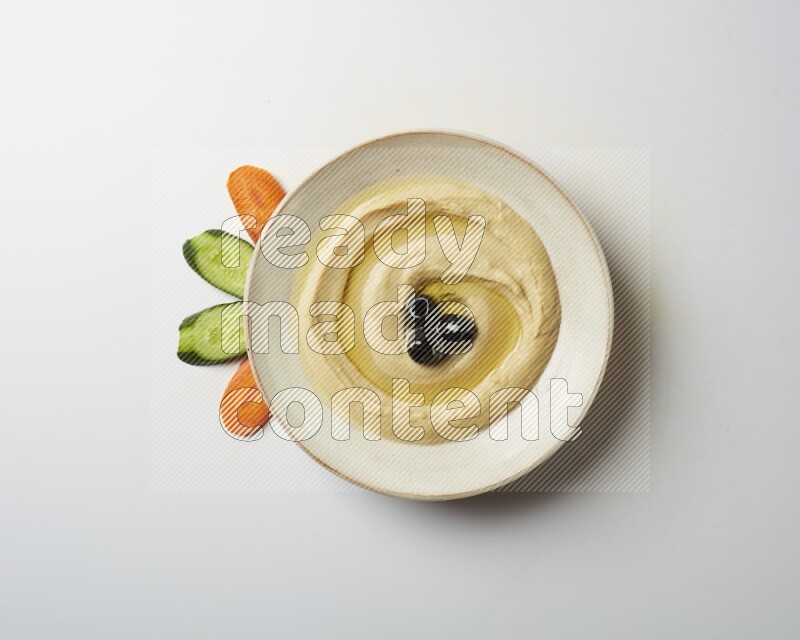 Hummus in a pottry plate garnished with black olives on a white background