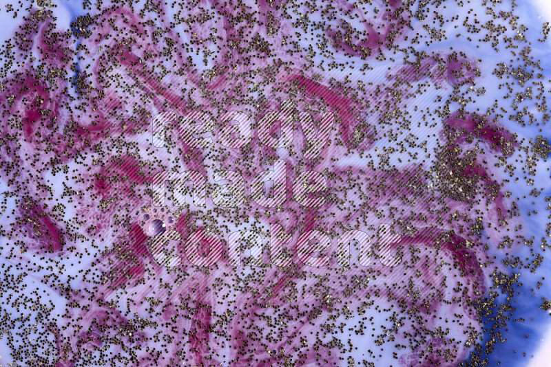 A close-up of sparkling gold glitter scattered on swirling blue and red background