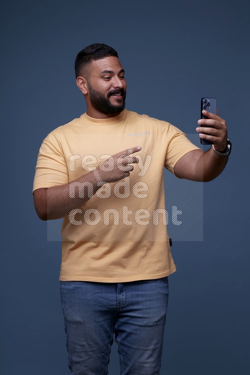 رجل يرتدي قميص اصفر باكمام قصيرة وبنطال جينز ازرق يقوم بمحادثة مرئية باستخدام جواله