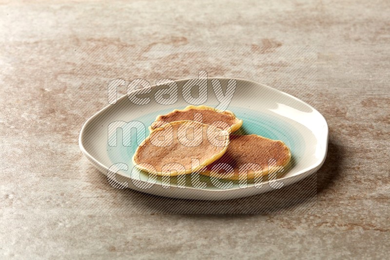 Three stacked plain mini pancakes in a bicolor plate on beige background