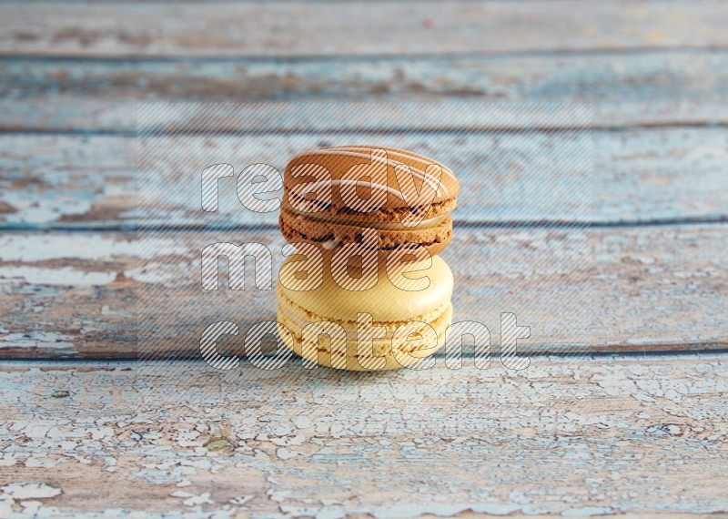 45º Shot of of two assorted Brown Irish Cream, and Yellow Vanilla macarons on light blue background