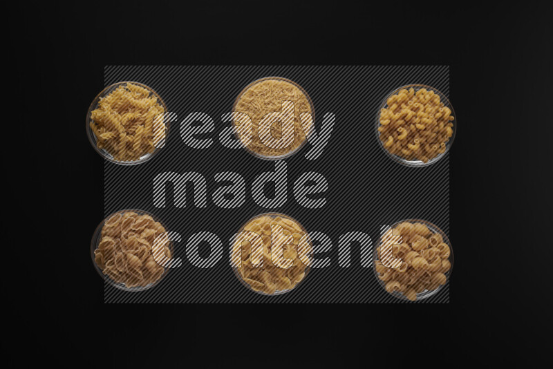 Different pasta types in 6 glass bowls on black background