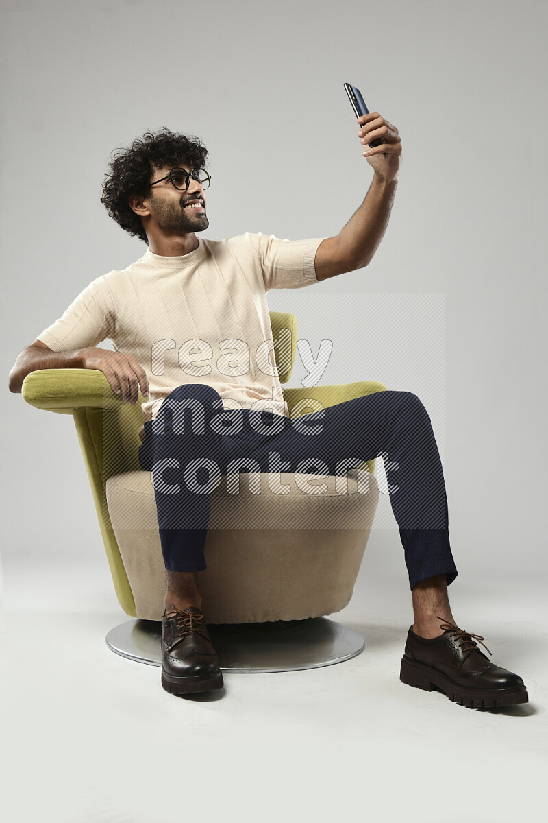 A man wearing casual sitting on a chair taking a selfie on white background