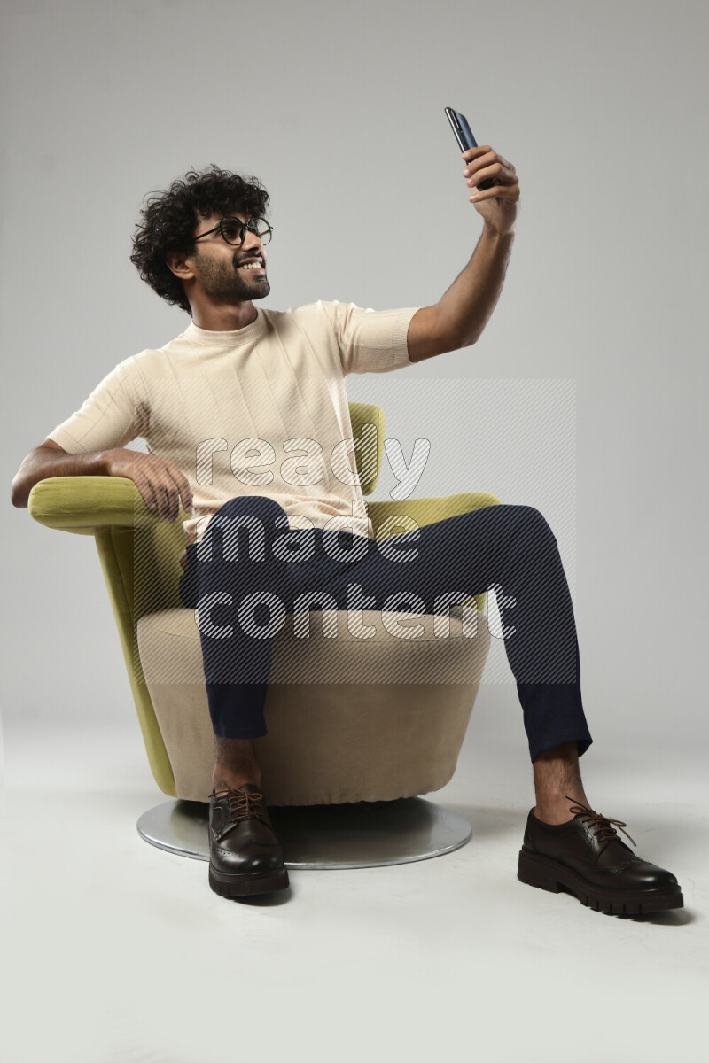 A man wearing casual sitting on a chair taking a selfie on white background