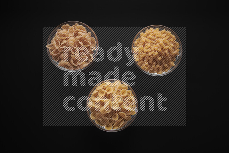 Different pasta types in glass bowls on black background