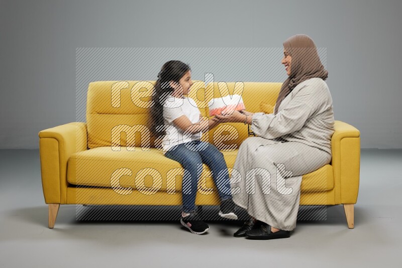 A girl sitting giving a cake to her mother on gray background