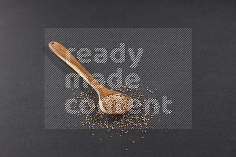 A wooden spoon full of mustard seeds on a black flooring