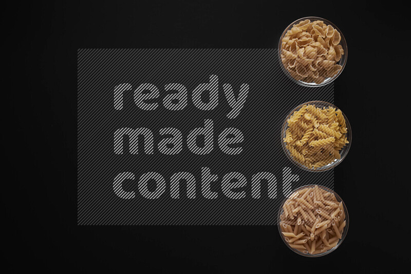 Different pasta types in 3 glass bowls on black background