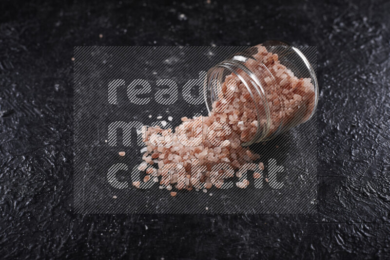 A glass jar full of coarse himalayan salt crystals on black background