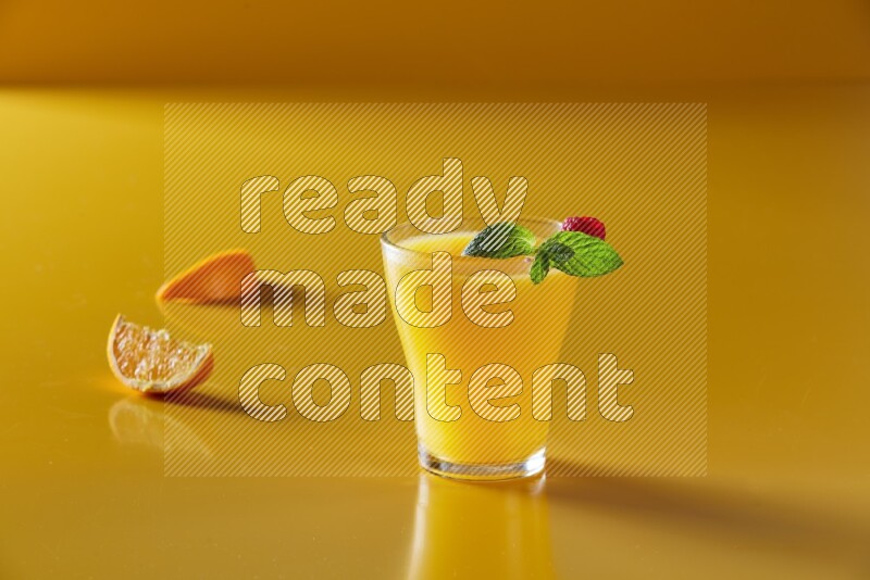 glass of orange juice with berry & mint on yellow background