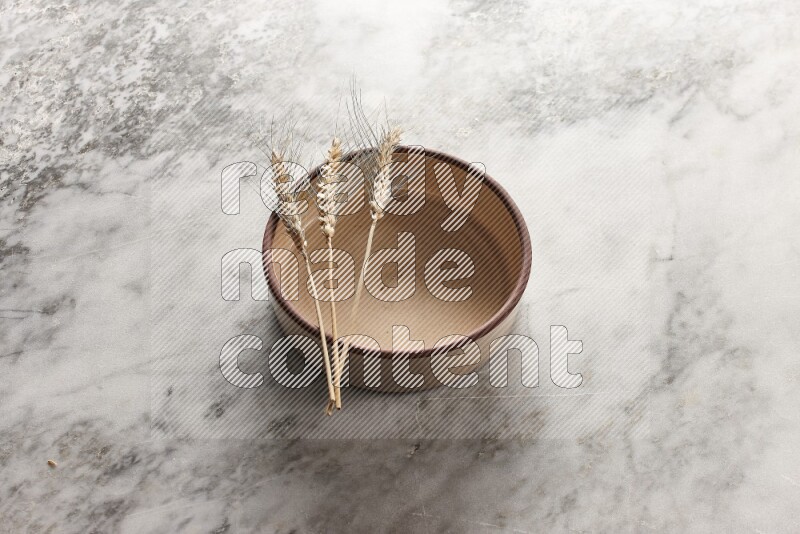 Wheat stalks on beige pottery oven bowl on grey marble background