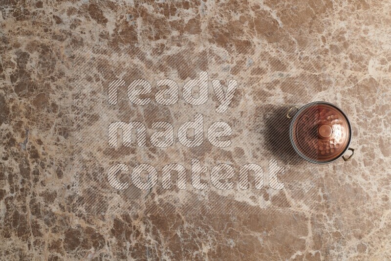 A small copper pot on beige marble background