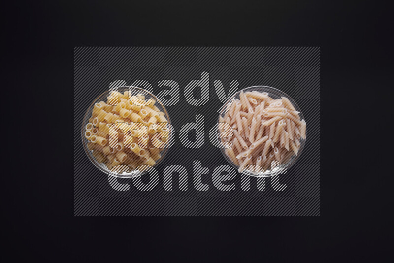 Different pasta types in glass bowls on black background