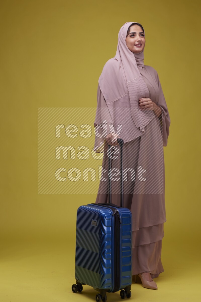 A woman With suit Case on a Yellow Background wearing Brown Abaya with Hijab