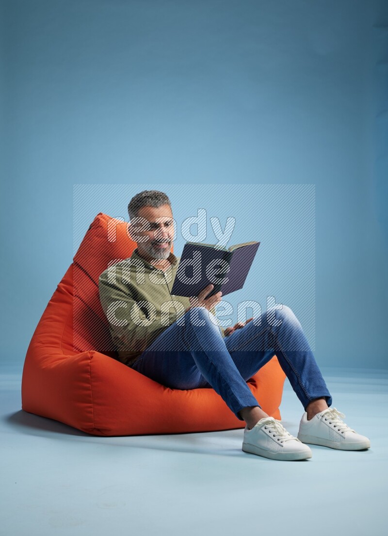 A man sitting on an orange beanbag and reading a book