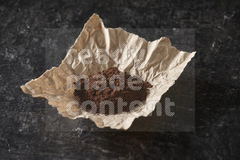 Cloves powder in crumpled piece of paper on a textured black flooring