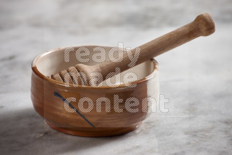Multicolored pottery bowl with wooden honey dipper in it on grey marble background