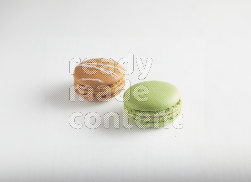45º Shot of of two assorted Brown Irish Cream, and Green Pistachio macarons on white background