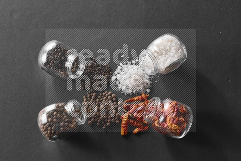 ملح وفلفل حار وفلفل أسود وحبوب الفلفل الحلو في أوعية زجاجية علي خلفية سوداء