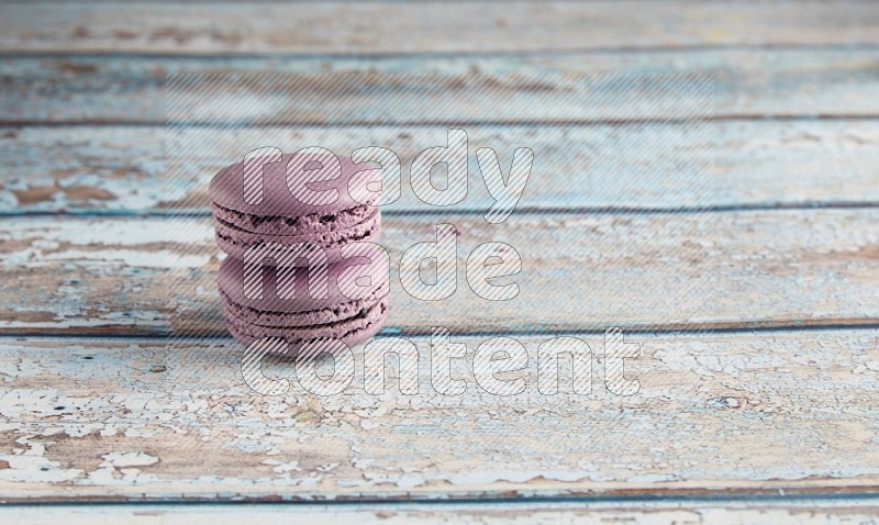 45º Shot of two Purple Blueberry macarons on light blue wooden background