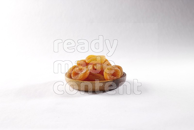 Dried apricots in a wooden bowl on white background