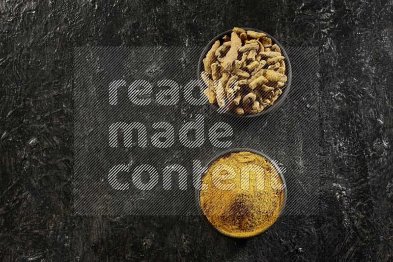 وعاءان من الفخار باللون الأسود، أحدهما ممتلئ ببودرة الكركم والآخر ممتلئ بأصابع كاملة من الكركم المجفف على خلفية سوداء